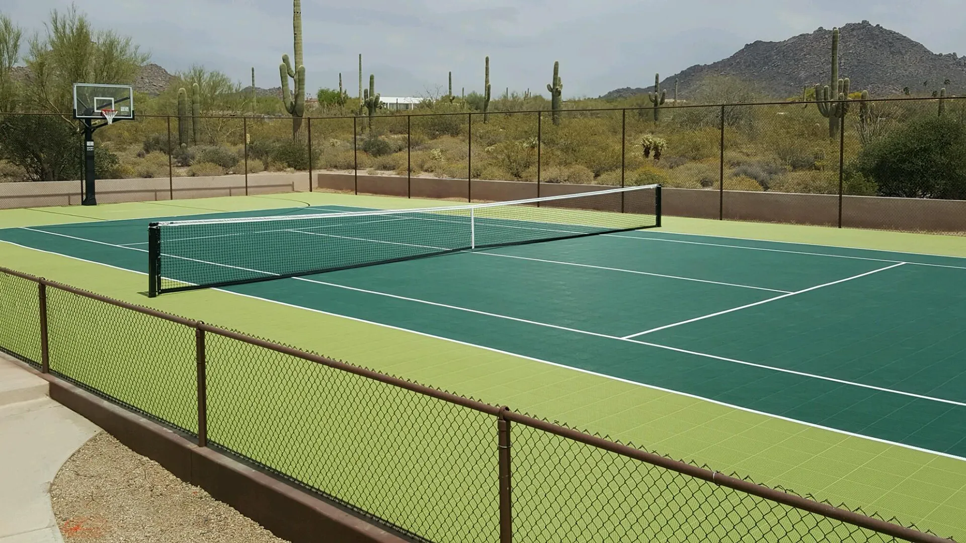 Green modular tile tennis court with basketball hoop